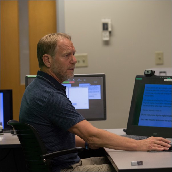 An instructor teaching from a distance classroom equipped with green screen and live video and audio recording devices.