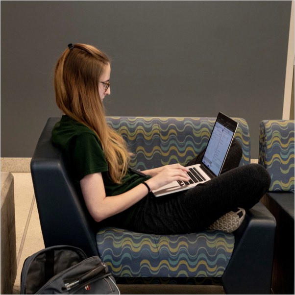 A student working remotely from a laptop while relaxing on a couch.